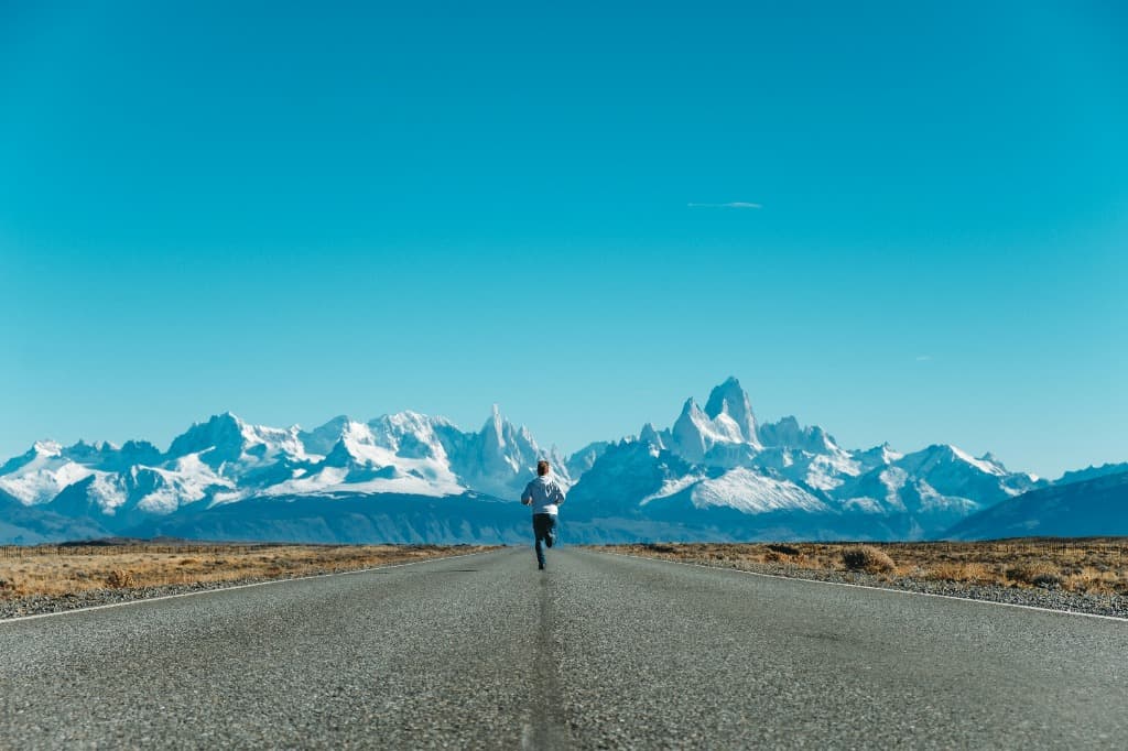 Trail runner on a straight road toward snow-capped Patagonian peaks